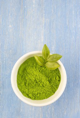 Kuru yeşil çay tozu kibrit çayı, beyaz bir fincanda tüm yapraklarla, mavi arka planda izole edilmiş. Çin şifalı çayı sağlık için sakinleştirir. Doğu çimeni