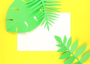 Sarı arka planda beyaz kağıt güneş gözlüklü, tropikal yapraklar, üst manzara. Kağıt yeşil yapraklı egzotik arkaplan