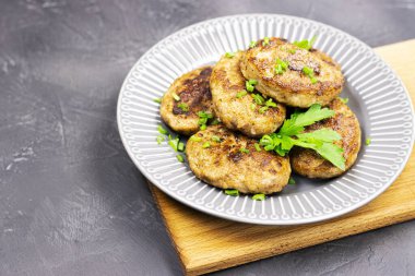 Tabağında yeşil sebzeler olan taze kızarmış pirzolalar, yakın plan. Siyah taş bir masanın üzerinde, ahşap bir standın üzerinde vahşi bir adamın yiyeceği.