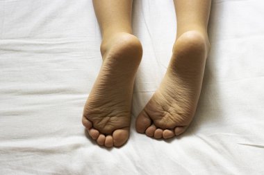 Beyaz bir yatağın üzerinde çocuk topukları. Düz tabanlı bir çocuk yatağında yatıyor.