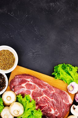 Çiğ mermer et bifteği ve koyu mermer arka planda baharatlar, üst manzara. Mantarlı taze yeşiller, sarımsak ve sığır eti.