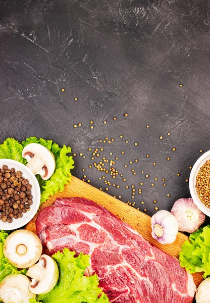 Raw fresh marble meat steak and seasonings on a dark marble background, top view. fresh greens with mushrooms, garlic and beef