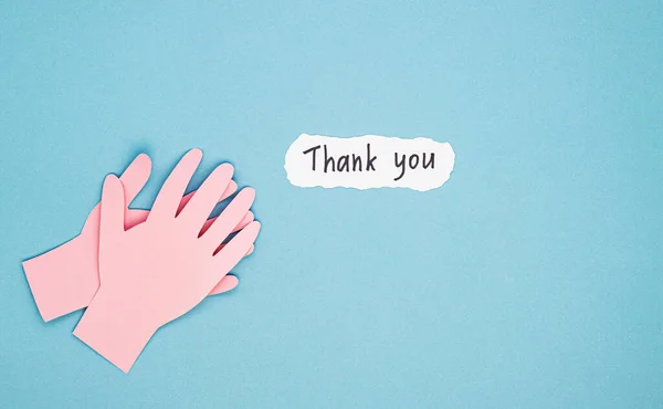 applauding paper hands and a thank you sign on a blue background. the concept of gratitude to doctors and nurses for their work