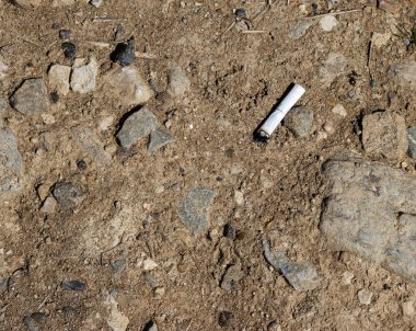 the butt of a white cigarette lies on a rocky surface, top view. environmental pollution