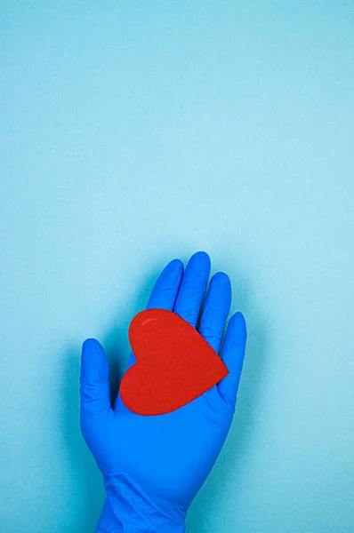 red heart in hand in a blue medical glove on a blue background. background for the day of the medic, top view, space for text