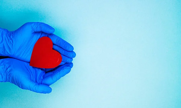 red heart in hands in blue medical gloves on a blue background. background for the day of the medic, top view, space for text