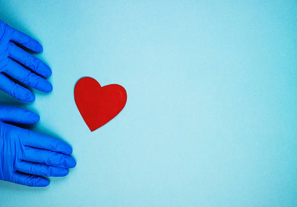 red heart and hands in blue medical gloves on a blue background. background for the day of the medic, top view, space for text