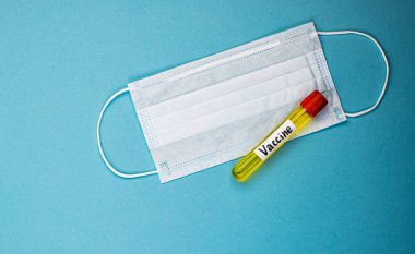 Covid-19 aşısını içeren bir ampul, virüsün tüm dünyaya yayılmasını engellemek için icat edildi. Mavi arka planda tıbbi maske