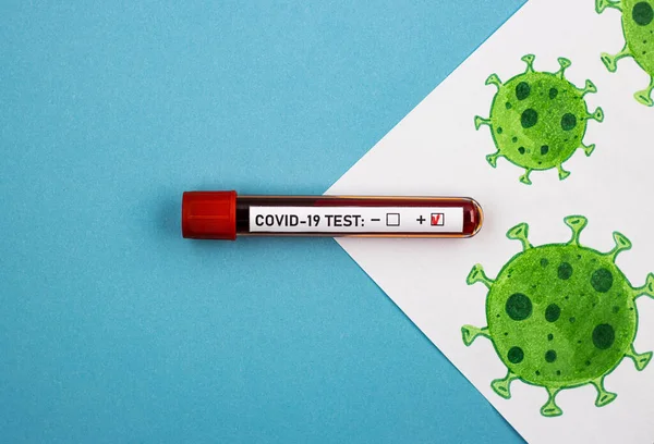 an ampoule with a positive test for covid-19 and a picture of the coronavirus on a blue background, top view. concept of blood donation for the coronavirus test