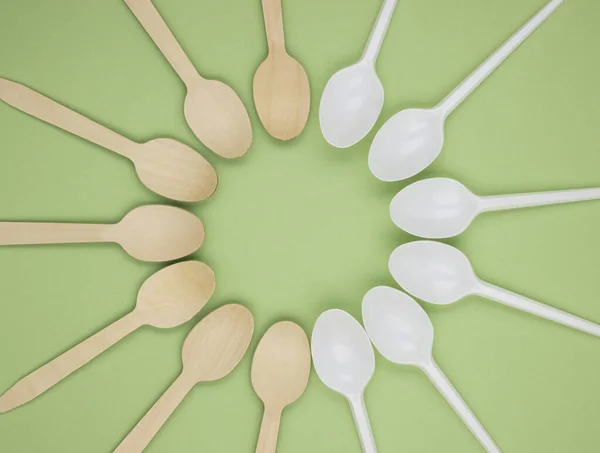 Disposable spoons made of bamboo wood and plastic on a green background. Spoons made of wood and plastic are arranged in a circle. The concept of zero waste. Preserving the purity of nature