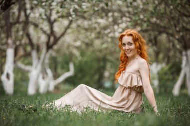 Bahçede bej elbiseli kızıl saçlı kız.