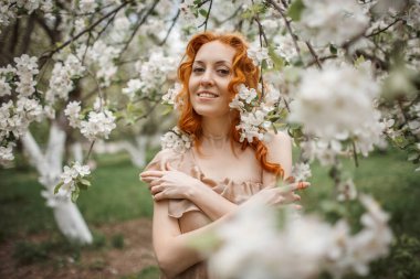 Bahçede bej elbiseli kızıl saçlı kız.