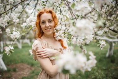 Bahçede bej elbiseli kızıl saçlı kız.