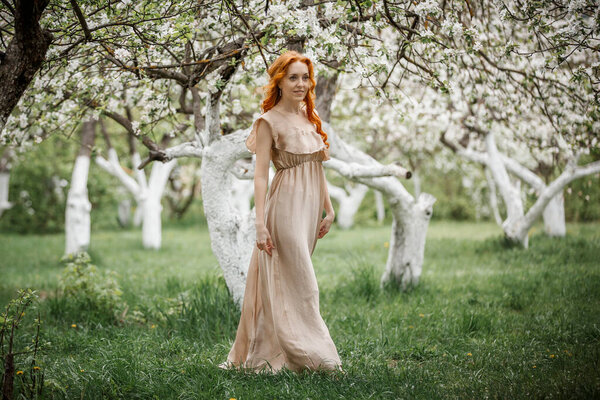 Red-haired girl in a beige dress in the garden