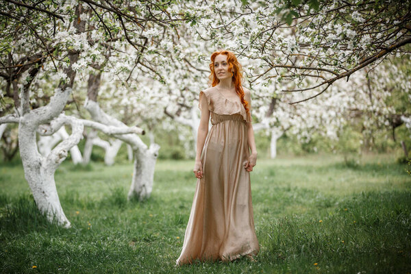 Red-haired girl in a beige dress in the garden