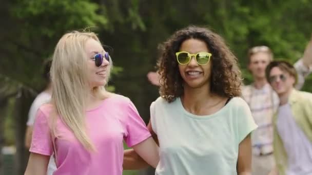 Enérgica pareja femenina bailando, sonriendo para la cámara, disfrutando de un picnic en el parque — Vídeo de stock