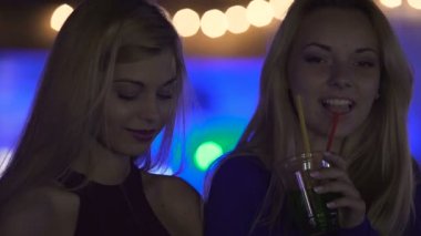 Flört eden genç kadınlar, mobil araçları kullanarak, partide kokteyl ve müzik zevk