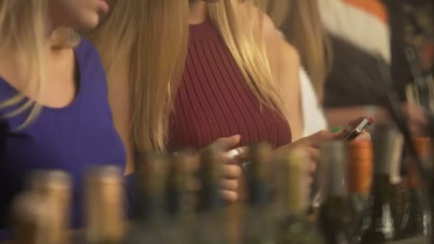 Flickorna chattar online vinflaskor använder smartphones, på bardisken i nattklubb — Stockvideo