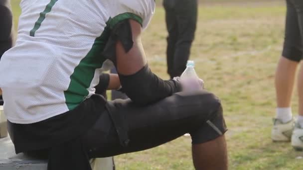 Durstiger Fußballer trinkt Wasser, ruht sich nach aktivem Spiel auf dem Feld aus — Stockvideo