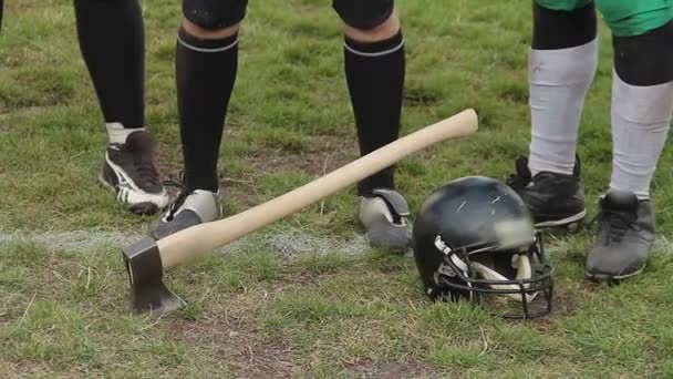 Axe stuck in gridiron field grass, football players ready to compete for trophy — ストック動画