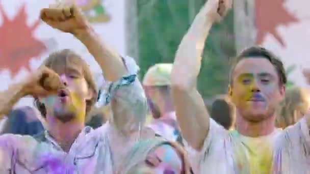 Beautiful woman and two men in powder paint jumping and dancing at Holi party — Stock Video