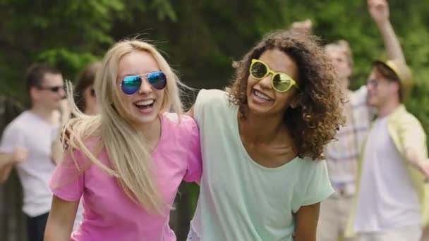 Студенты веселятся в парке, две красивые многорасовые девушки танцуют, улыбаются — стоковое видео