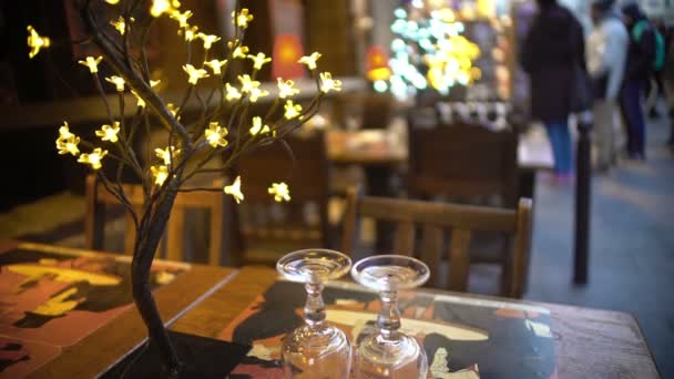 Ambiente romántico en la cafetería de la calle, copas de vino e instalación iluminada — Vídeos de Stock