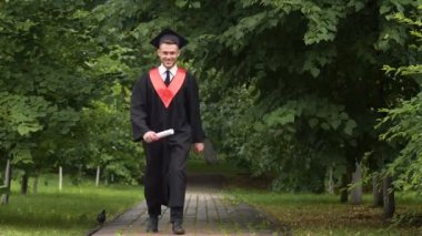 Elinde, diploma taşıyan akademik elbiseli genç adam ile sevinç atlama gülümseyen