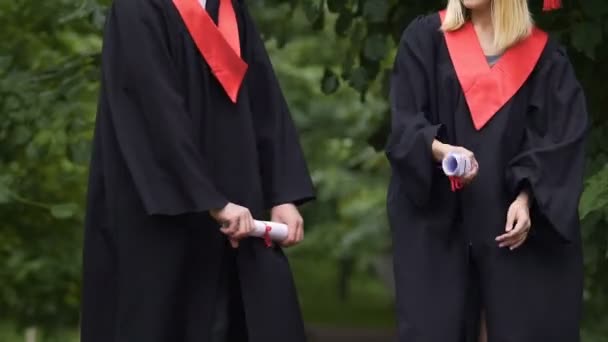 Vrolijke mannelijke en vrouwelijke afgestudeerden gek rond en diploma's in handen te houden — Stockvideo