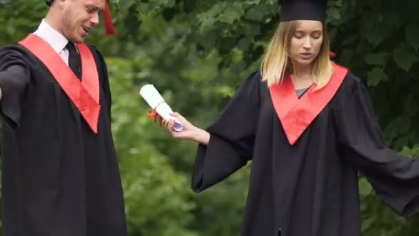 Graduados engraçados em vestidos acadêmicos dançando e cantando no parque perto da universidade — Vídeo de Stock