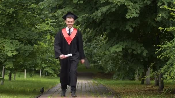Usmíval se mladý muž v akademické šaty nosili diplom v rukou, skákání s radostí