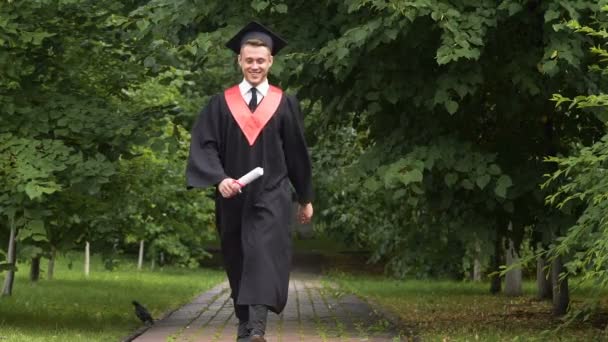 Щасливий чоловік випускник ходить в парку, стрибає з радістю, успіхом і майбутнім — стокове відео