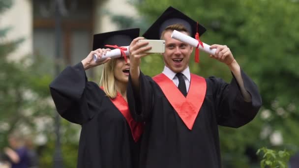 Afgestudeerde studenten in academische jurken selfies nemen na graduatie ceremonie — Stockvideo