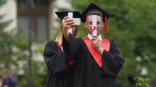 Divertidos graduados hombres y mujeres tomando selfie después de la graduación, celebrando — Vídeo de stock