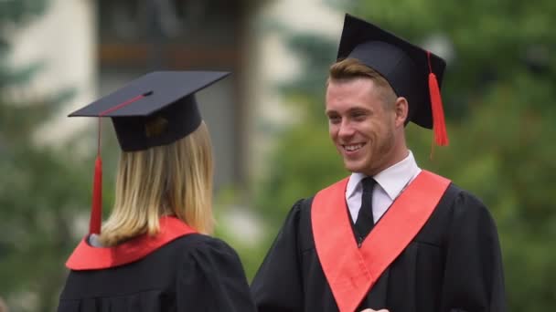 Молоді випускники обіймаються після церемонії випуску, красиві усміхнені люди — стокове відео