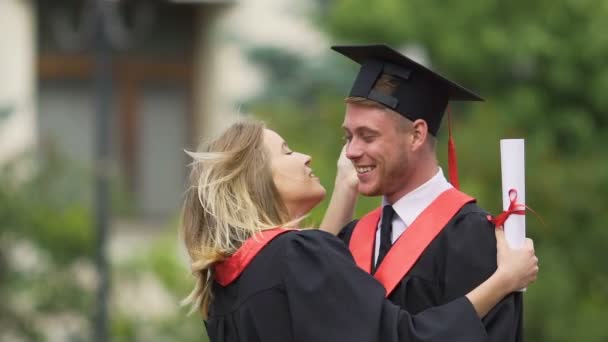 Красивая девушка обнимает и целует своего парня, счастливые выпускники наслаждаются жизнью — стоковое видео