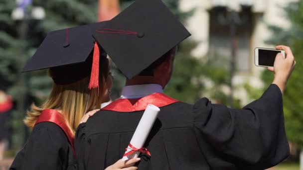 Lachende mannelijke en vrouwelijke afgestudeerden nemen selfie, geluk, succesvolle toekomst — Stockvideo