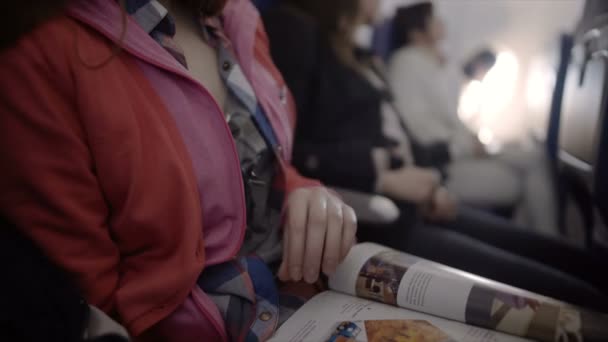 Giovane donna che gira pagine di rivista lucida mentre vola in aereo passeggero — Video Stock