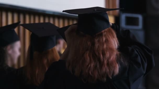 Senhoras femininas ajustando cabelo e bonés acadêmicos, cerimônia de formatura universitária — Vídeo de Stock