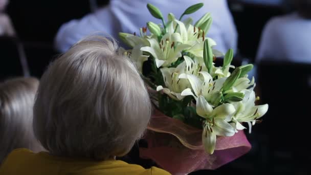 Елегантна старша леді дивиться концерт, тримаючи купу красивих квітів лілії — стокове відео