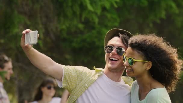 Молодая пара обнимается и делает селфи, тусуется с друзьями на вечеринке — стоковое видео