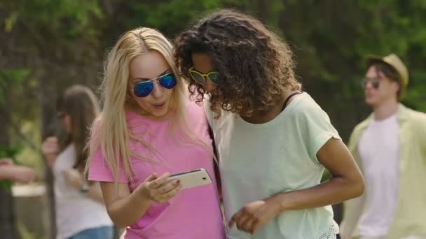 Junge schöne Frauen sehen Fotos auf dem Smartphone im Park, Party, entspannen — Stockvideo