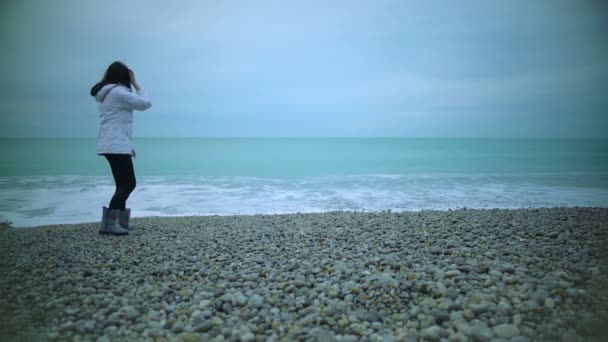 Menina bonita jogando seixos no mar e desfrutando de uma boa vista, salpicando água — Vídeo de Stock