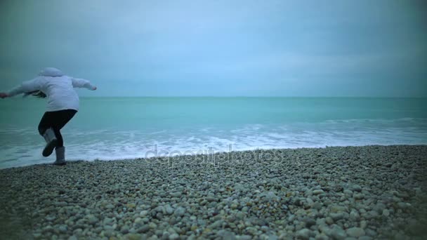 Молодая женщина ходит по пляжу, боится мокрой обуви в морской воде, брызги волн — стоковое видео