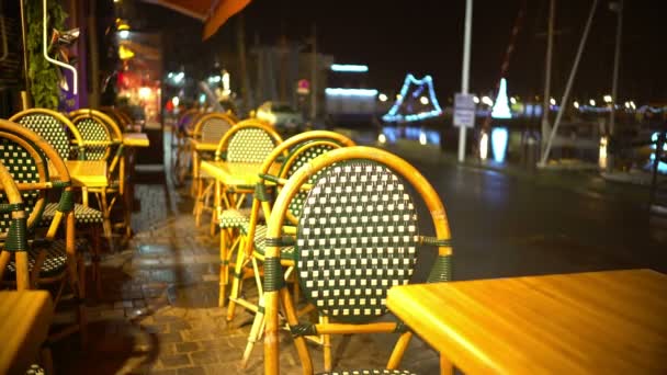 Tables and chairs of empty street restaurant, people walking by, rainy night — Stock Video