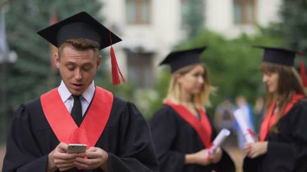 Мужчина выпускник чтение хорошие новости на смартфоне перед церемонией, удивление — стоковое видео