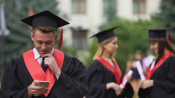 Χαρούμενα απόφοιτος διαβάζοντας καλές ειδήσεις στο smartphone και χαμογελώντας, αποφοίτηση — Αρχείο Βίντεο