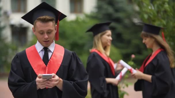 Feliz graduado masculino en el manto eligiendo hotel para vacaciones de verano en el teléfono inteligente — Vídeo de stock