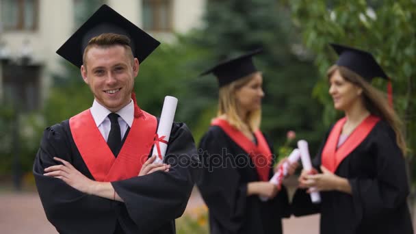 Guapo graduado masculino sonriendo para la cámara con los brazos cruzados, futuro feliz — Vídeo de stock