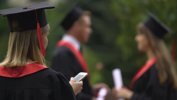 Blondynka w akademickich cap sukienka i podziałka surfowanie w sieci na smartphone — Wideo stockowe